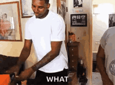 A Man In A White T-Shirt Is Standing In A Room With A Dog . GIF