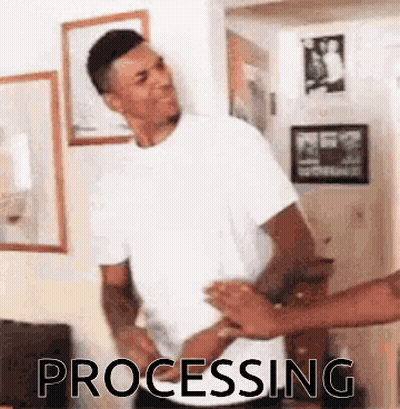 A Man In A White T-Shirt Is Standing In A Room With A Group Of People Standing Around Him . GIF