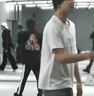 A Man In A White T-Shirt Is Standing In Front Of A Mirror In A Room . GIF