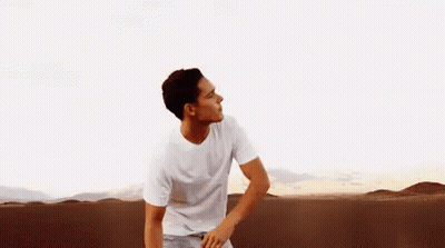 A Man In A White T-Shirt Is Standing In The Middle Of A Desert . GIF