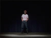 A Man In A White T-Shirt Is Standing On A Stage GIF