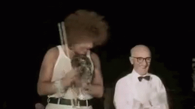 A Man In A White Tank Top And A Man In A Bow Tie Are Dancing On A Stage . GIF
