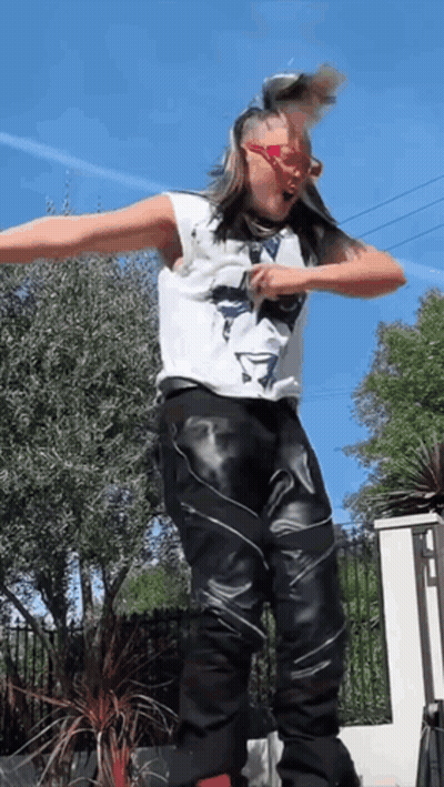 A Man In A White Tank Top And Black Leather Pants Is Jumping In The Air GIF