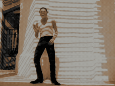 A Man In A White Tank Top And Black Pants Is Standing In Front Of A Building GIF