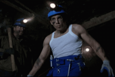 A Man In A White Tank Top And Blue Pants Is Standing In A Dark Cave GIF