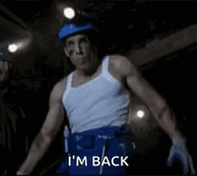 A Man In A White Tank Top And Blue Shorts Is Standing In A Dark Room And Says `` I 'M Back '' GIF