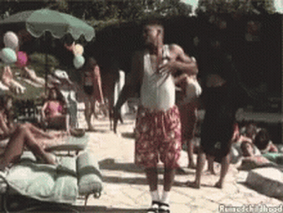A Man In A White Tank Top And Red Shorts Is Dancing In Front Of A Group Of People GIF