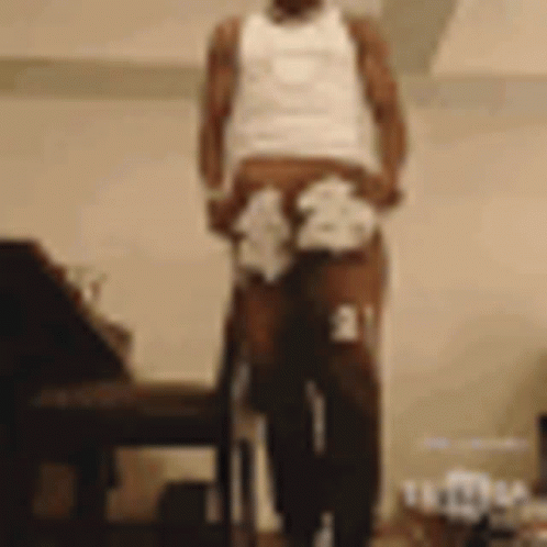 A Man In A White Tank Top And Underwear Is Standing Next To A Chair Holding A Cane . GIF