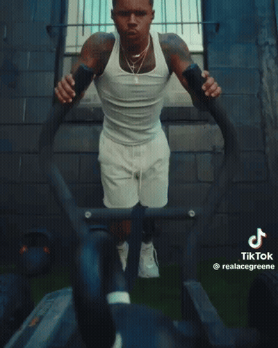 A Man In A White Tank Top And White Shorts Is Doing Push Ups On A Machine That Says Tik Tok GIF