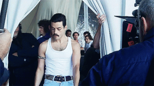 A Man In A White Tank Top Is Being Photographed By A Man In A Blue Shirt GIF