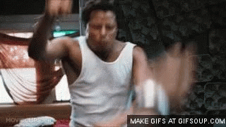 A Man In A White Tank Top Is Dancing In A Room With His Hands In The Air . GIF