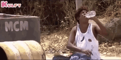 A Man In A White Tank Top Is Drinking Water From A Bottle . GIF