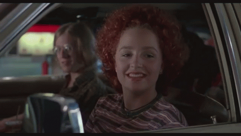 A Man In A White Tank Top Is Driving A Car With Another Man Sitting In The Back Seat GIF