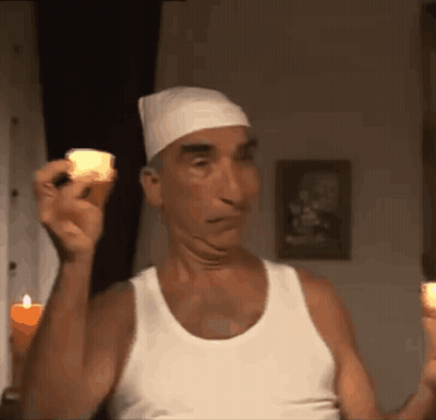 A Man In A White Tank Top Is Holding Two Lit Candles GIF