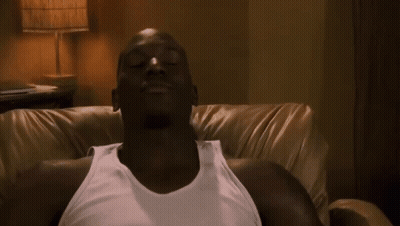 A Man In A White Tank Top Is Laying On A Couch With His Eyes Closed GIF
