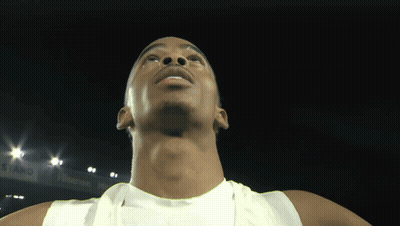A Man In A White Tank Top Is Looking Up At The Camera GIF