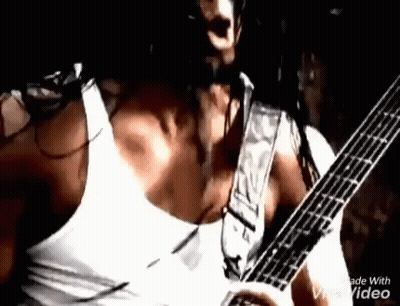 A Man In A White Tank Top Is Playing A Guitar On Stage . GIF