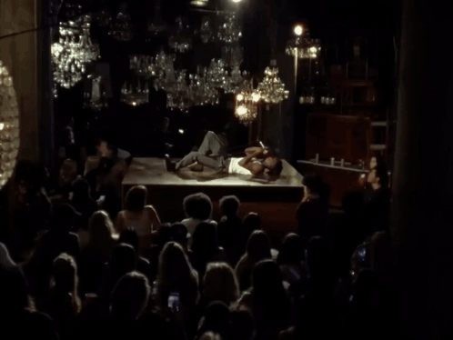 A Man In A White Tank Top Is Singing Into A Microphone GIF