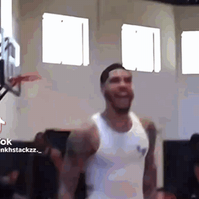 A Man In A White Tank Top Is Smiling In A Gym . GIF