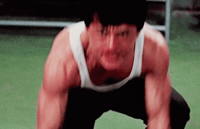 A Man In A White Tank Top Is Squatting Down And Making A Funny Face GIF