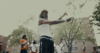 A Man In A White Tank Top Is Standing In A Park With A Group Of People . GIF