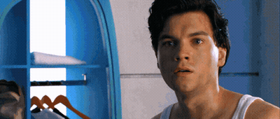 A Man In A White Tank Top Is Standing In Front Of A Closet GIF