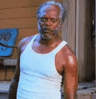 A Man In A White Tank Top Is Standing In Front Of A Door . GIF