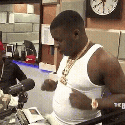 A Man In A White Tank Top Is Standing In Front Of A Microphone In A Room . GIF