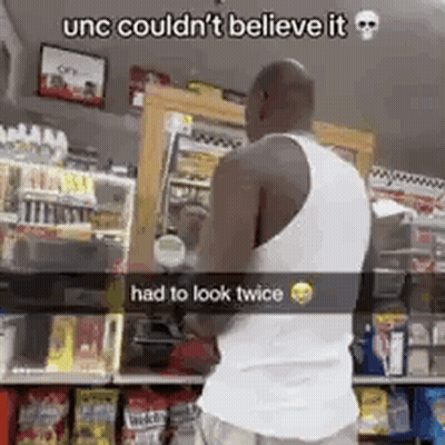 A Man In A White Tank Top Is Standing In Front Of A Store . GIF
