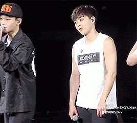 A Man In A White Tank Top Is Standing Next To Another Man In A Black Jacket . GIF