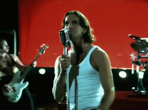 A Man In A White Tank Top Singing Into A Microphone GIF