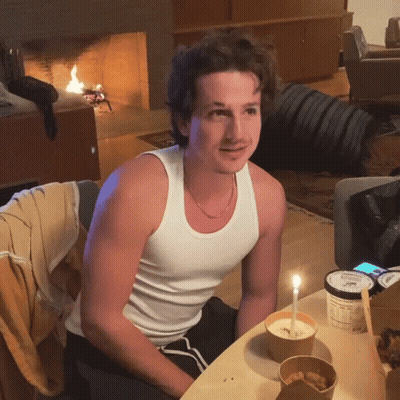 A Man In A White Tank Top Sits At A Table With A Container Of Ice Cream GIF