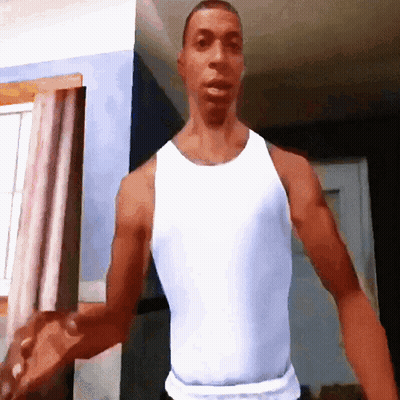 A Man In A White Tank Top Stands In A Room GIF