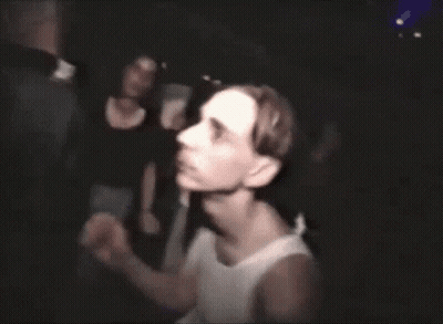 A Man In A White Tank Top Stands In Front Of A Group Of People GIF