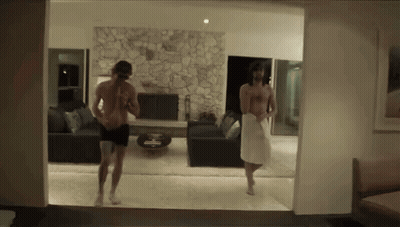 A Man In A White Towel Is Walking In A Living Room GIF