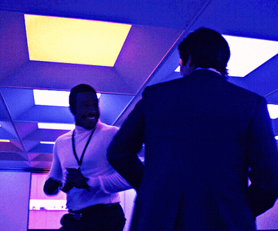 A Man In A White Turtleneck Is Standing Next To Another Man In A Black Suit GIF