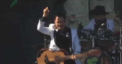 A Man In A White Tuxedo Is Playing A Guitar On Stage GIF