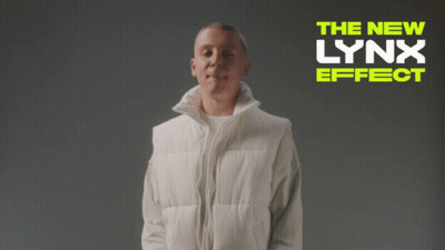 A Man In A White Vest Is Standing In Front Of A Banner That Says The New Lynx Effect GIF