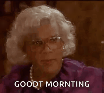 A Man In A Wig And Glasses Is Sitting Down And Saying `` Good Morning '' . GIF