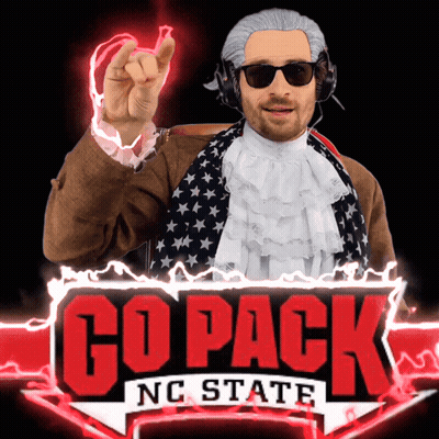 A Man In A Wig And Sunglasses Stands In Front Of A Go Pack Nc State Sign GIF