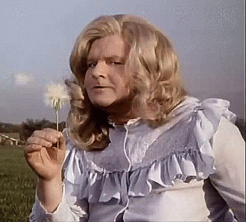 A Man In A Wig Is Blowing A Dandelion In The Air . GIF