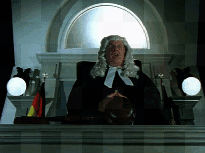 A Man In A Wig Is Holding A Judge 'S Gavel In Front Of A Window GIF