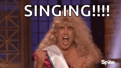 A Man In A Wig Is Singing While Wearing A Sash . GIF