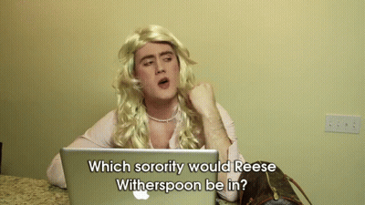 A Man In A Wig Is Sitting In Front Of An Apple Laptop And Asking Which Sorority Would Reese Witherspoon GIF
