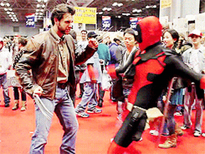 A Man In A Wolverine Costume Stands Next To A Woman In A Deadpool Costume At A Convention GIF