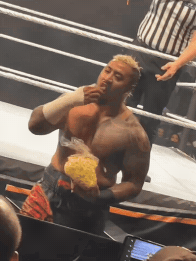 A Man In A Wrestling Ring Holds A Bag Of Chips In His Hand GIF