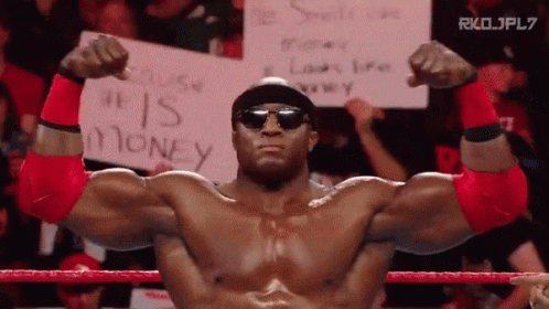 A Man In A Wrestling Ring Holds A Sign That Says " He Is Money " GIF