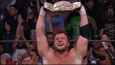 A Man In A Wrestling Ring Is Holding A Championship Belt Above His Head GIF