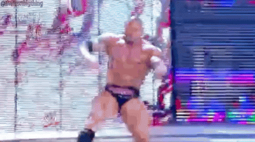 A Man In A Wrestling Trunks Is Dancing In Front Of A Screen . GIF