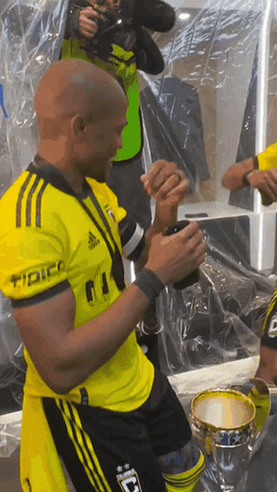 A Man In A Yellow Adidas Shirt Holds A Cup In His Hand GIF